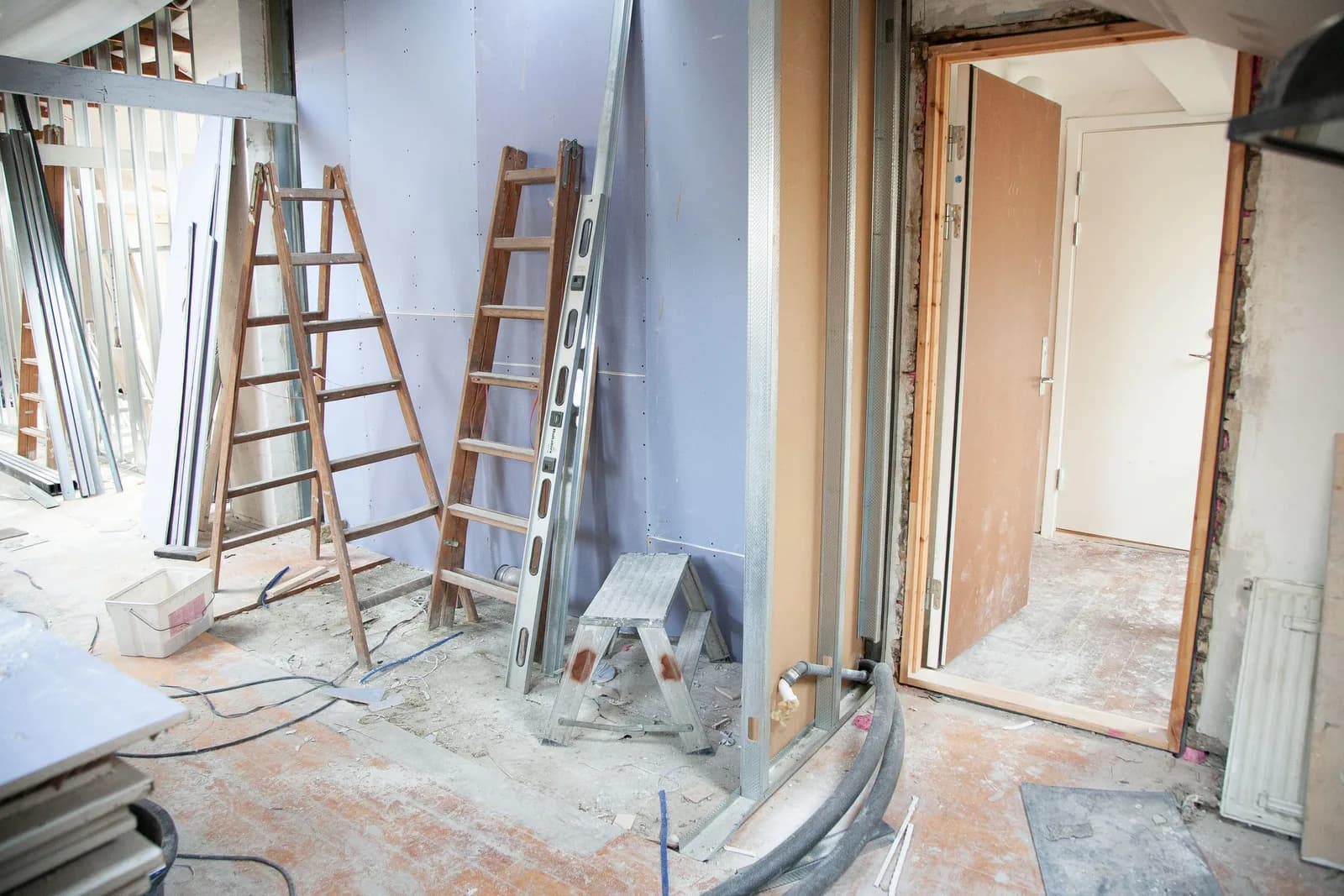 Habitación en obra con escaleras de mano, tabiques de placa y una puerta recién colocada
