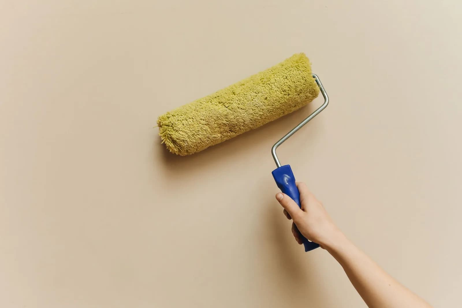 Mano pasando un rodillo de pintura por una pared lisa
